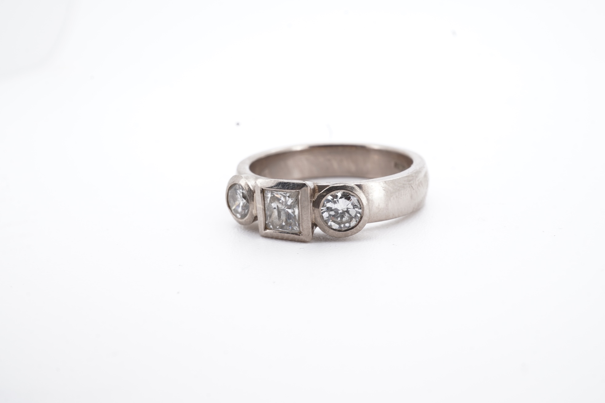 A modern 18ct white gold and three stone diamond ring, set with single square cut diamond and two round cut diamonds, size K, gross weight 5.8 grams.